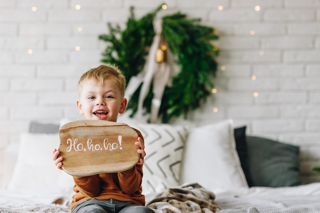 Ragazzo caucasico felice sveglio che apre i suoi regali la mattina di Natale Corona dell'albero di Natale sullo sfondo Bambino eccitato e sorridente Buone vacanze in famiglia a casa Apertura dei regali in scatole Copia spazio