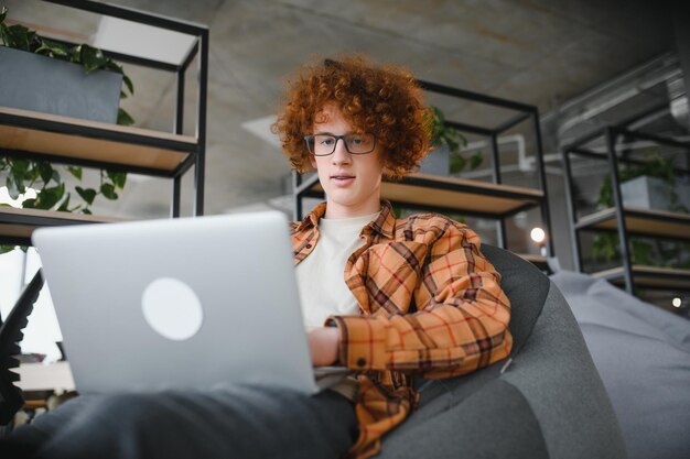 Ragazzo caucasico hipster che gode di un lavoro a distanza in una caffetteria Libero professionista maschio in occhiali alla moda seduto in caffetteria con un moderno dispositivo portatile