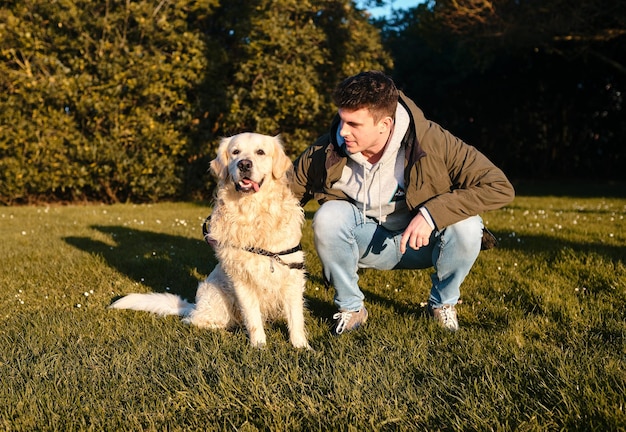 Ragazzo caucasico in piedi con un cane golden retriever in un parco verde