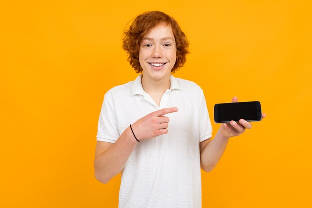 Ragazzo caucasico in una camicia bianca con uno smartphone con un modello in bianco su un giallo con lo spazio della copia