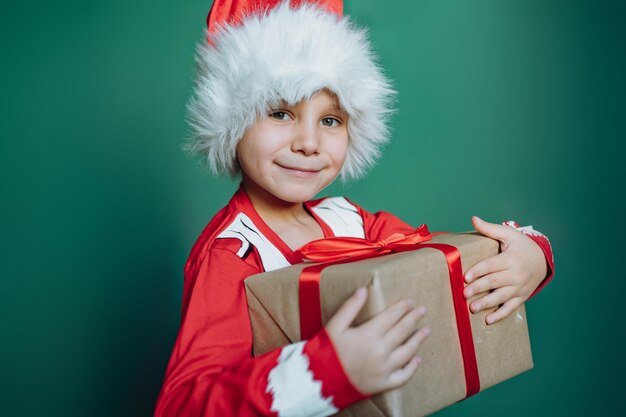 Ragazzo caucasico sorridente felice in maglietta e cappello della Santa che tiene una scatola con il regalo di natale