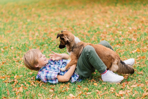 Ragazzo che abbraccia un cane e gioca con in autunno, parco cittadino