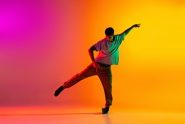 Foto ragazzo che balla hip-hop in abiti eleganti su sfondo sfumato nella sala da ballo alla luce al neon.
