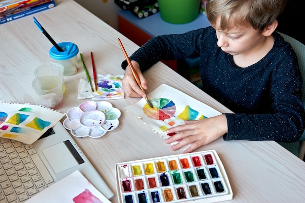 Ragazzo che dipinge immagini con colori ad acquerello durante la lezione d'arte. Allievo sul disegno con il pennello. Ruota dei colori e tavolozza dell'acquerello. Lezioni hobby per principianti di teoria del colore