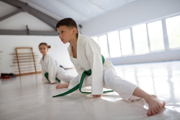 Ragazzo che fa spaccatura. Ragazzo dai capelli scuri che fa spaccare la gamba mentre allunga le gambe prima dell'aikido