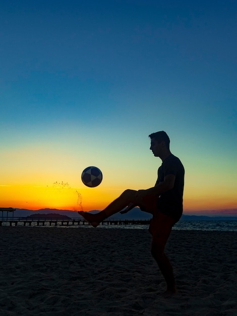 Ragazzo che fa sport con la palla sulla spiaggia in piena estate tramonto sulla costa brasiliana