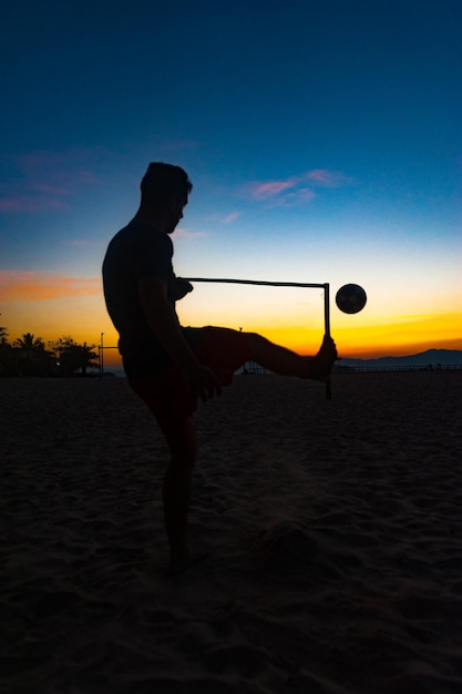 Ragazzo che fa sport con la palla sulla spiaggia in piena estate tramonto sulla costa brasiliana