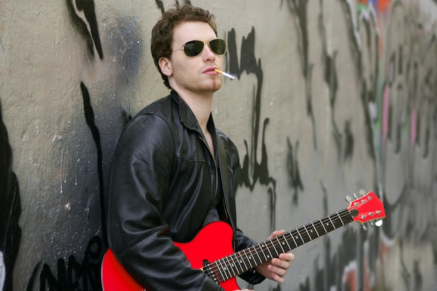 Ragazzo che fuma la sigaretta rock in pelle a suonare la chitarra