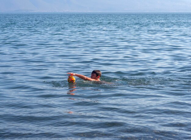 Ragazzo che gioca a palla sulla spiaggia del Mar Egeo su un'isola greca in una giornata estiva in Grecia