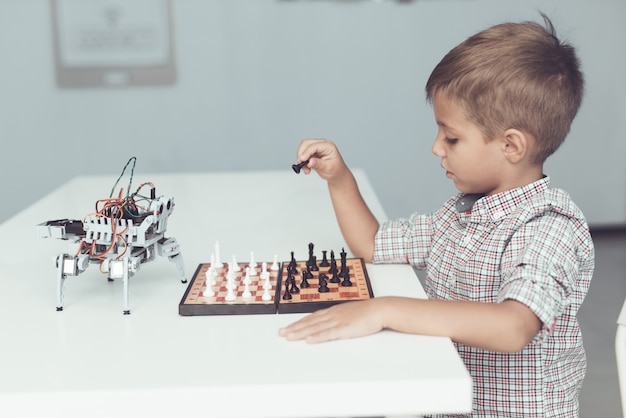 Ragazzo che gioca a scacchi con un piccolo robot al tavolo.