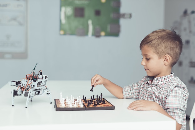 Ragazzo che gioca a scacchi con un piccolo robot al tavolo.