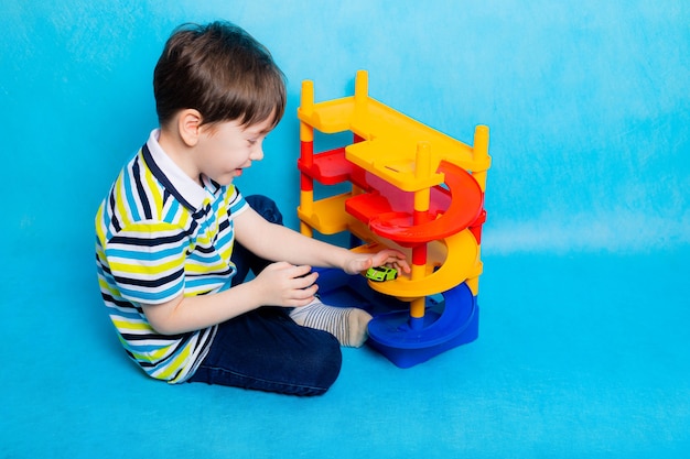 Ragazzo che gioca con le auto nel parcheggio. Giocattolo per bambini. Un ragazzo gioca il gioco Parcheggio su una superficie blu Parcheggio luminoso per auto. Infanzia felice