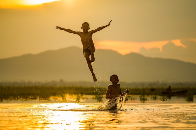 Ragazzo che gioca spruzzi d'acqua nel fiume durante il tramonto, spruzzi d'acqua, Thailandia