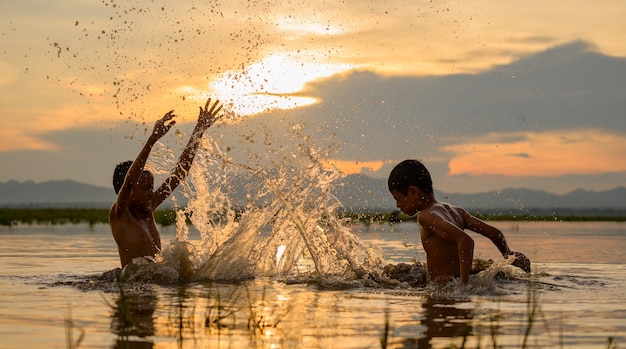 Ragazzo che gioca spruzzi d'acqua nel fiume durante il tramonto, spruzzi d'acqua, Thailandia