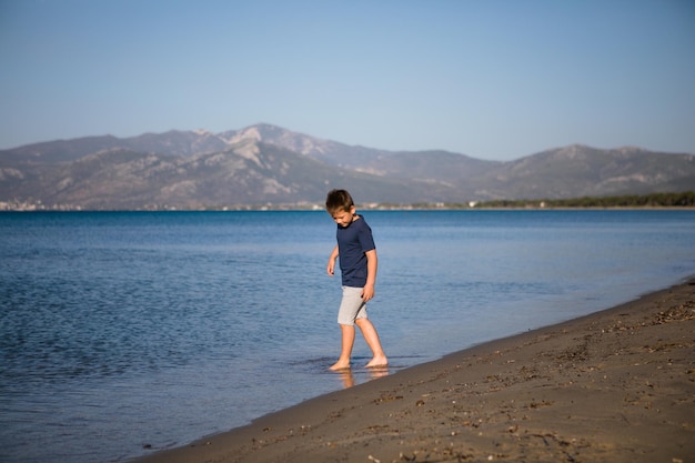 Ragazzo che gioca sulla spiaggia durante le vacanze estive Bambini in natura con una bellissima sabbia di mare e blu che corre nell'acqua di mare