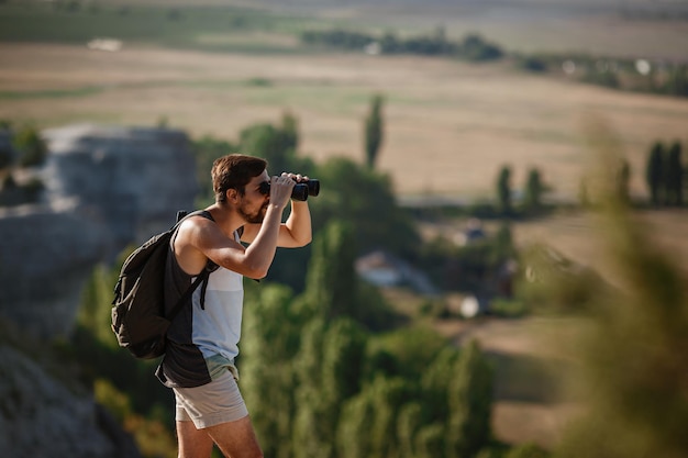 Ragazzo che guarda il binocolo in collina uomo in maglietta con zaino