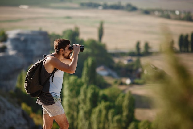 Ragazzo che guarda il binocolo in collina uomo in maglietta con zaino