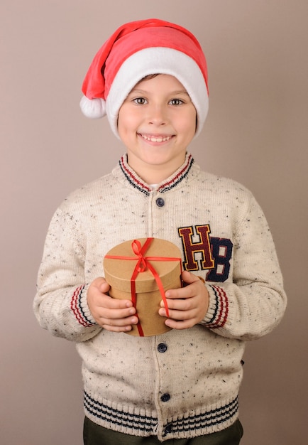 Ragazzo che indossa il cappello di Babbo Natale che tiene un regalo su uno sfondo beige