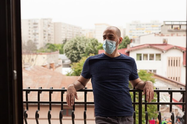 Ragazzo che indossa una maschera medica che si rilassa sul balcone durante la pandemia globale.