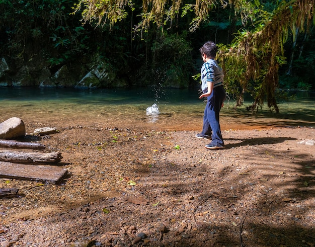 Ragazzo che lancia pietra nel fiume nella foresta pluviale