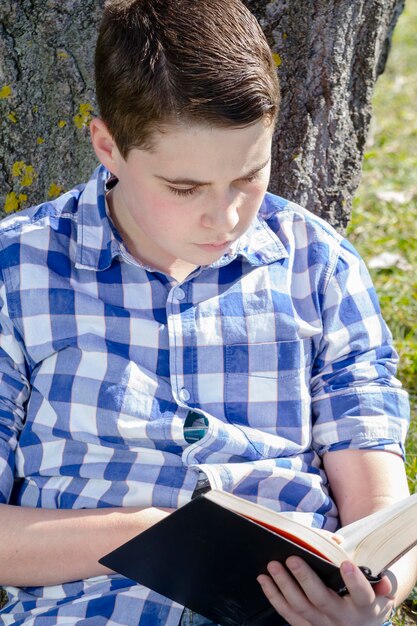 Ragazzo che legge un libro nel bosco con profondità di campo ridotta e spazio di copia