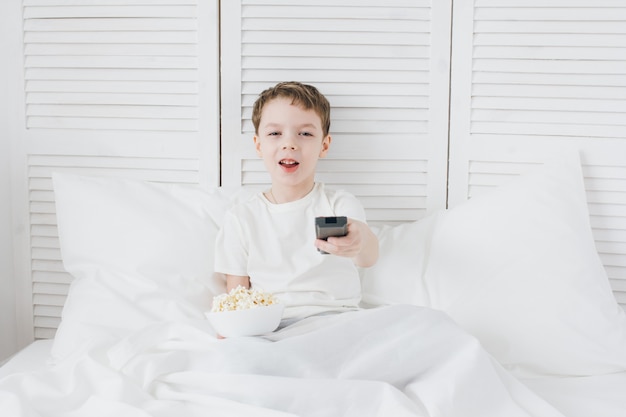 Ragazzo che mangia popcorn seduto nel letto e guardare la TV