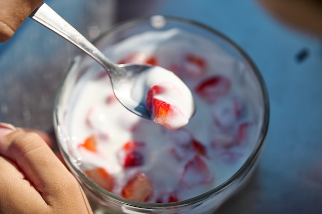 Ragazzo che mangia uno yogurt naturale con fragole in una ciotola con un cucchiaio d'argento, non vengono mostrate facce