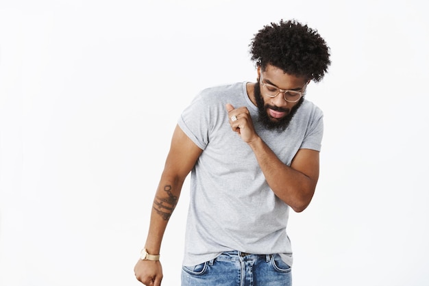 ragazzo che mostra le mosse di danza mentre si diverte a godersi la musica, celebrando il successo e vincendo agitando la testa guardando i piedi spensierato e fresco, posando felice sul grigio.