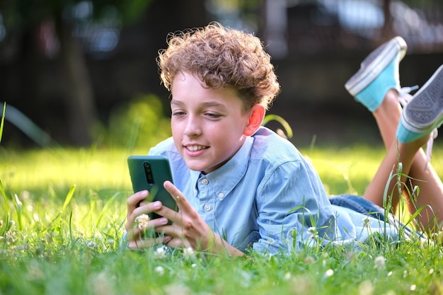 Ragazzo che naviga nel suo smartphone all'aperto nel parco estivo. Utilizzo del cellulare per il tempo libero e il concetto di istruzione.