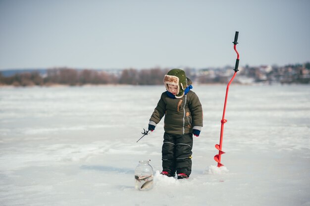 Ragazzo che pesca in inverno. Il ragazzo sveglio cattura i pesci nel lago d'inverno. Inverno. All'aperto