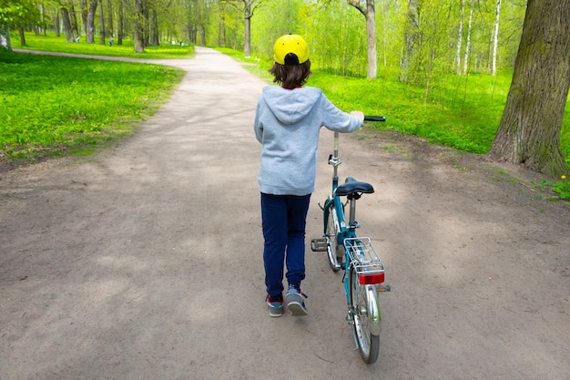 Ragazzo che porta la bici nelle vicinanze lungo il sentiero in vista del parco dal retro