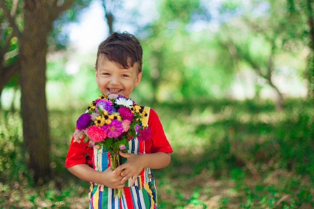 Ragazzo che ride con un mazzo di fiori selvatici nelle sue mani sullo sfondo della festa della mamma della natura