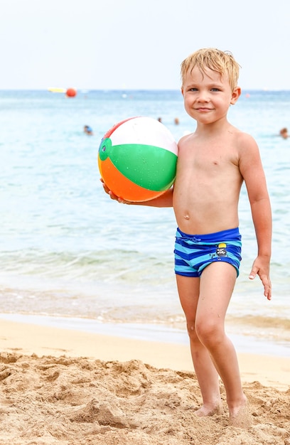 Ragazzo che ride eccitato che tiene pallone da spiaggia colorato in spiaggia godendosi le vacanze estive