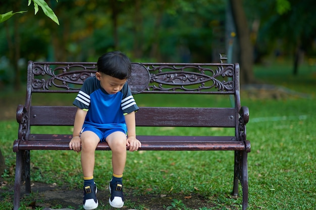 Ragazzo che si siede sul parco del banco con umore triste nel concetto di depressione del bambino