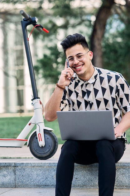 Ragazzo che studia in un parco con un laptop e uno scooter