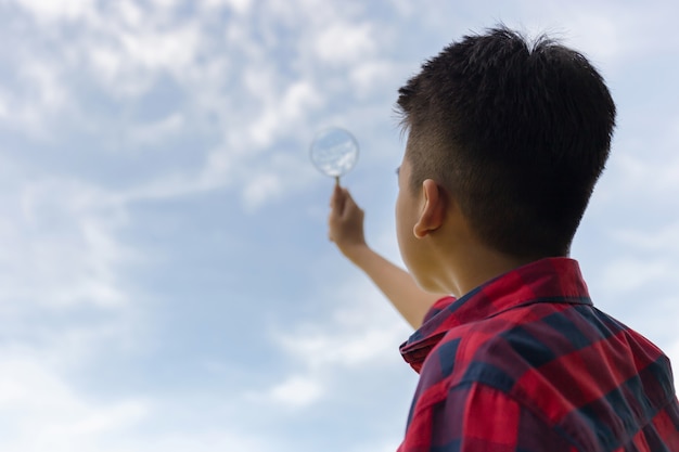 Ragazzo che tiene una lente d'ingrandimento e che guarda al cielo