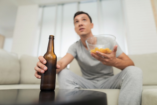 Ragazzo con birra e patatine guardando la TV.