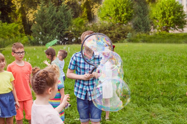 Ragazzo con gli amici che fanno grandi bolle di sapone all'aperto sul prato verde