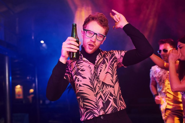 Ragazzo con gli occhiali beve birra I giovani si divertono nel night club con luci laser colorate