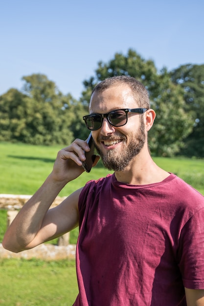 Ragazzo con gli occhiali da sole che sorride e che parla con cellulare