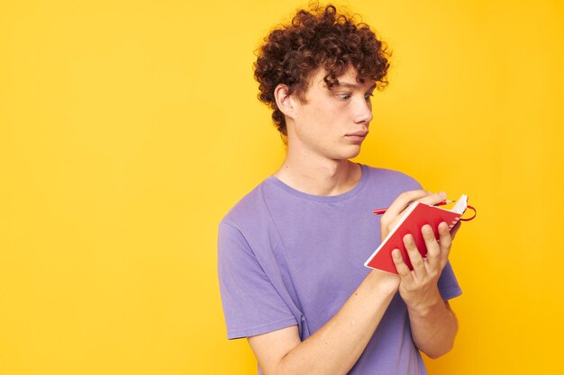 Ragazzo con il blocco note dei capelli ricci rossi con la penna che impara le emozioni sfondo giallo inalterato