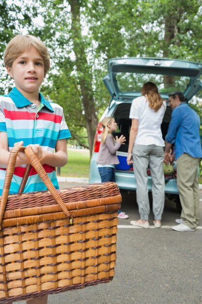 Ragazzo con il cestino di picnic mentre famiglia nella priorità bassa al circuito di collegamento di automobile