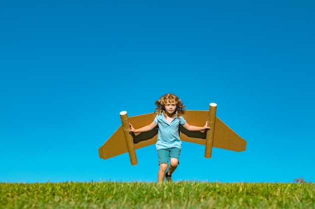 Ragazzo con il pilota del bambino del supereroe del jet pack sullo sfondo del cielo estivo ragazzo con il volo dell'aereo di carta verso