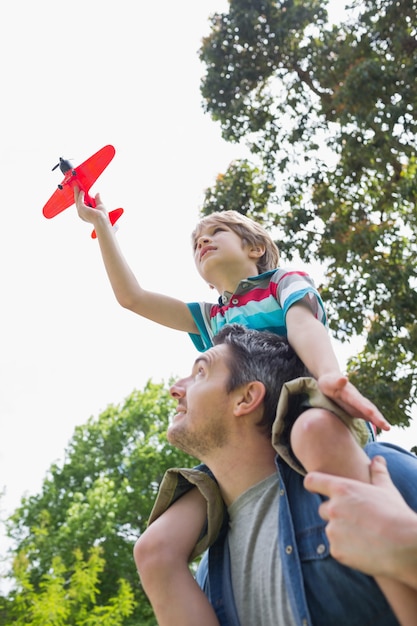 Ragazzo con l&#39;aeroplano del giocattolo che si siede sulle spalle del padre