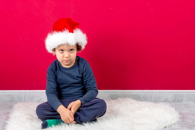 Ragazzo con l'espressione seria che si siede con il cappello di natale