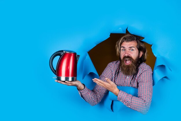 Ragazzo con la barba che beve tè brutale hipster caucasico con bollitore elettrico bere bevanda calda di buona qualità sorpreso assistente di negozio uomo maturo che presenta utensile da cucina