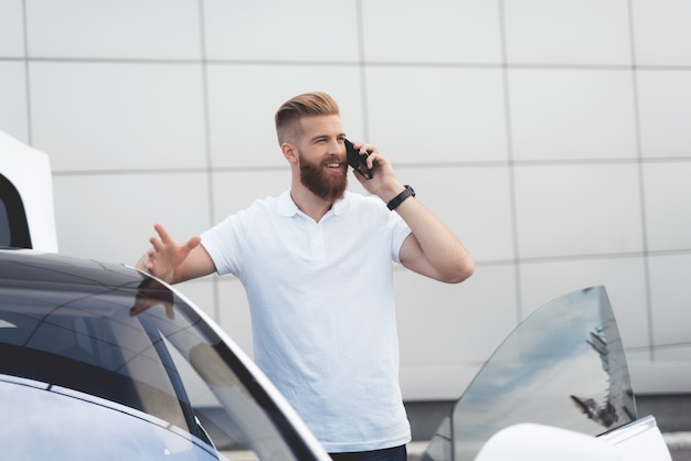 Ragazzo con la barba che parla al telefono vicino alla sua auto elettrica