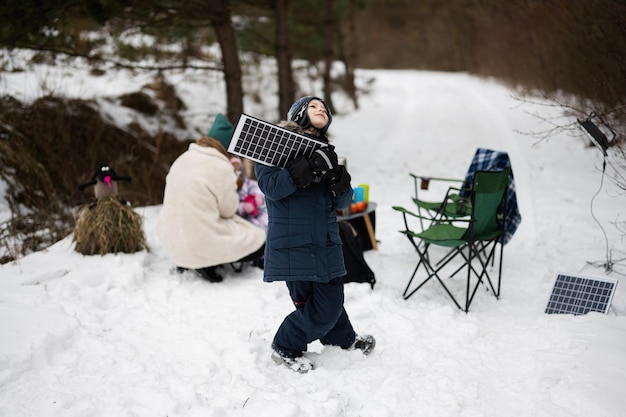 Ragazzo con la batteria del pannello solare a portata di mano contro la sua famiglia nella foresta invernale