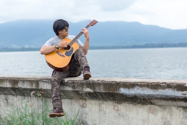 Ragazzo con la chitarra in piedi sulla diga, pantaloni cargo