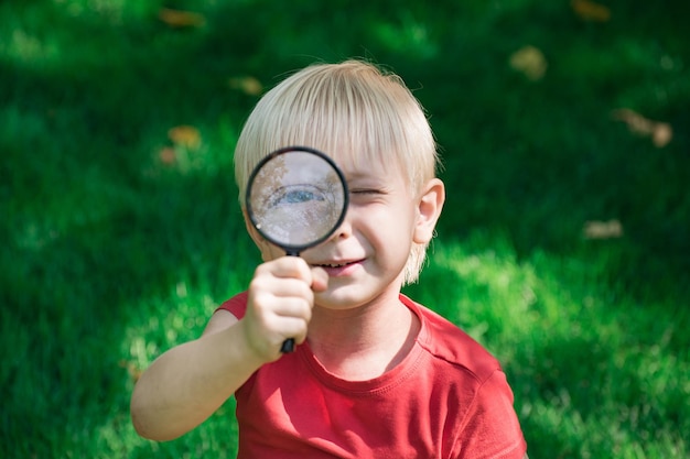 Ragazzo con la lente d'ingrandimento all'aperto Visione di scoperta dell'indagine